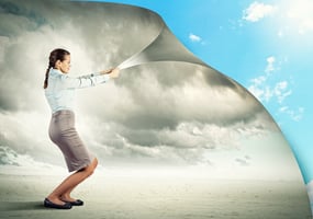 A professionally dressed woman pulls back a curtain, revealing a bright blue sky behind a previously grey, overcast scene. This visually represents the theme of the blog post, "Why Losing Your Job Can Be an Opportunity (And How to Make the Most of It)," symbolizing a fresh start, optimism, and new possibilities after job loss.